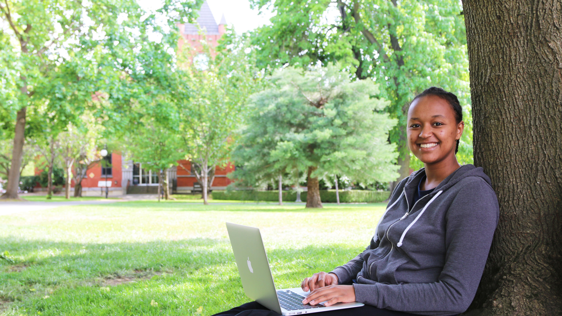 Female student sitting under a tree with a laptop on lap
